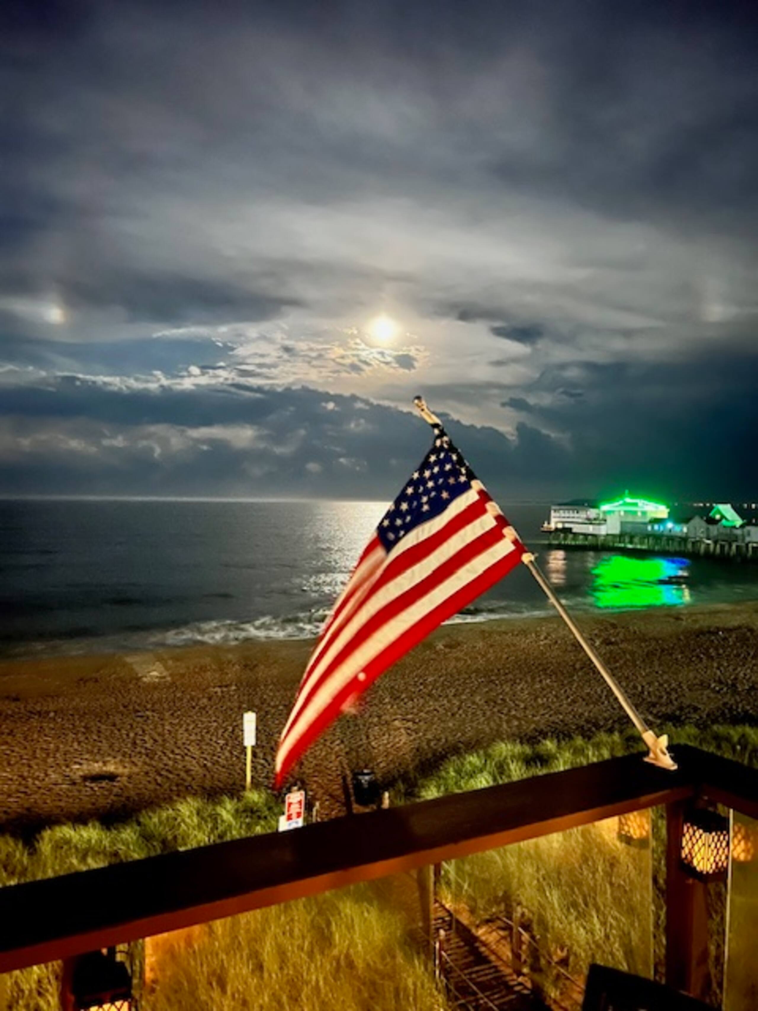American flag under a moonlit night sky by the pier